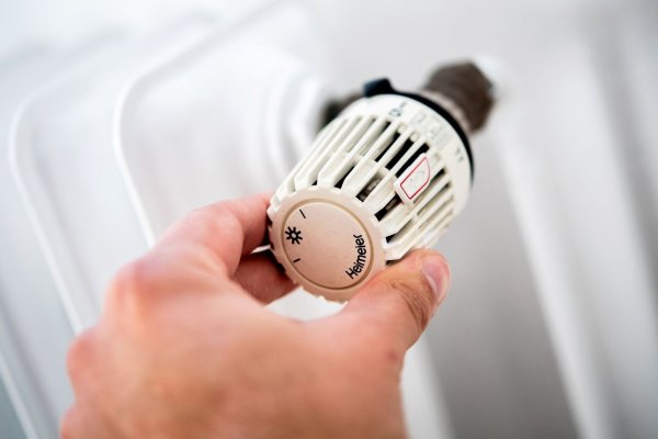 Ein Mann dreht in einer Wohnung am Thermostat einer Heizung. - © Hauke-Christian Dittrich/dpa/Symbolbild