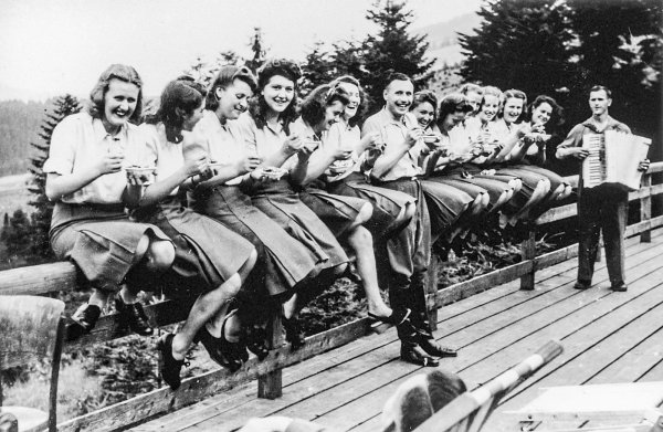Fröhliches Lachen in die Kamera: Junge SS-Helferinnen und Karl-Friedrich Höcker (Mitte) löffeln auf der Terrasse des SS-Ferienheimes in der Nähe von Auschwitz genießerisch Blaubeeren aus einem Schälchen. - © United States Holocaust Memorial Museum
