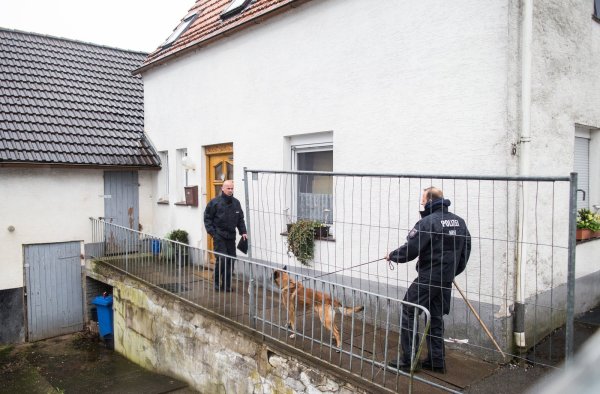 Ermittlungen vor Ort: Ein Polizist mit einem Hund an der Leine auf dem Grundstück vor dem Haus des beschuldigten Ehepaares in Höxter-Bosseborn. - © dpa