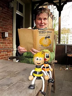 B&auml;rbel Bitter liest aus "Die Biene Maja und ihre Abenteuer" vor - Ausgabe 439 aus dem Jahr 1926. Sie sitzt vor dem Ellenhof, wo Autor Waldemar Bonsels einmal lebte. - &copy; FOTO: KURT EHMKE