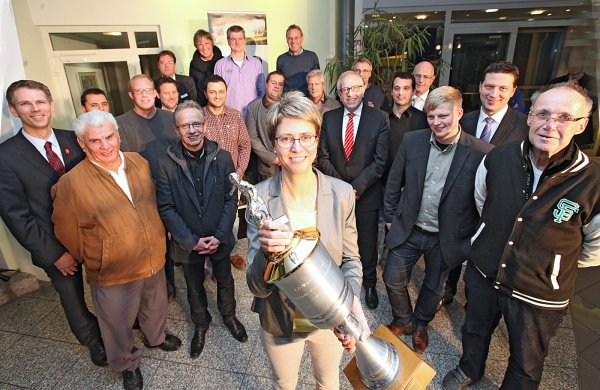 Um diesen Pokal geht es: Kirsten Bröker (LZ-Marketing) hält den LZ-Cup in der Hand. Zudem freuen sich Sponsoren, Organisatoren und die Delegierten der Vereine auf dei Endrunde in der Lemgoer Lipperlandhalle.  - © Gerstendorf-Welle