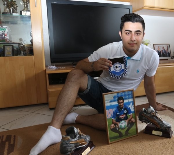 Ein Foto vor dem Trophäenschrank: Nujin Hassan präsentiert stolz das Bild, das ihn im Arminia-Trikot zeigt. Hinter ihm sind etliche Pokale zu sehen. - © Oliver König