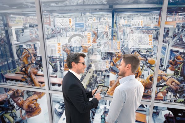 Menschen kommunizieren mit Kollegen anderer Disziplinen und den intelligenten Robotern in der Smart Factory. An der Glasscheibe sind die Kontroll- und Steuerungselemente zu erkennen. - © Weidmüller