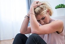 Junge Frau sitzt traurig auf dem Fu&szlig;boden einer Wohnung - Christin Klose/dpa-tmn