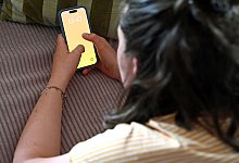 Frau liegt auf dem Sofa und schaut auf ein Smartphone - Elisa Schu/dpa/dpa-tmn