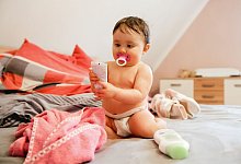 Ein Baby sitzt in Windeln im Bett - Mascha Brichta/dpa-tmn