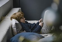 Redheaded boy lying on couch looking at cell phone - picture alliance / Westend61