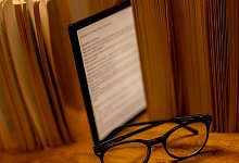 E-Book-Reader steht zwischen Büchern auf einem Tisch - Monika Skolimowska/dpa/dpa-tmn