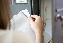 Eine Frau öffnet am Briefkasten einen Brief - Christin Klose/dpa-tmn