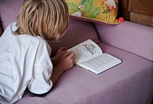 Kind liest, während es auf der Couch liegt - Annette Riedl/dpa/dpa-tmn