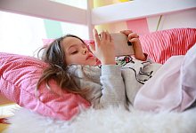 Ein Kind liegt im Bett und hat ein Smartphone in der Hand - Mascha Brichta/dpa-tmn