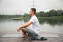 Ein Mann sitzt im Schneidersitz auf einem Steg - Christin Klose/dpa-tmn