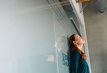 Eine Frau lehnt ersch&ouml;pft an einer Glaswand im B&uuml;ro - Zacharie Scheurer/dpa-tmn