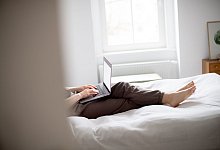 Eine Frau sitzt mit Laptop im Bett - Zacharie Scheurer/dpa-tmn