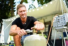 Ein junger Mann schliesst eine Gasflasche an einen Grill an - Tobias Hase/dpa-tmn/dpa