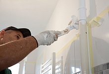 Maler lackiert mit weißer Farbe ein Rohr - Kai Remmers/dpa-tmn