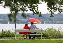 Renter sitzen mit einem Schirm am See - Thomas Warnack/dpa/dpa-tmn