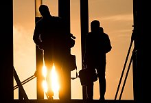 Zwei Männer gehen mit Aktentasche bei Sonnenaufgang über Brücke - Julian Stratenschulte/dpa/dpa-tmn