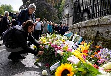 Menschen legen Blumen und letzte Gr&uuml;&szlig;e in der N&auml;he von Schloss Balmoral nieder. Doch nicht alle trauern um die K&ouml;nigin, zumal nicht in ehemaligen Kolonien. - Alastair Grant/AP/dpa