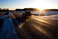Auto fährt bei Sonnenaufgang über eine spiegelglatte Landstraße - Julian Stratenschulte/dpa/dpa-tmn