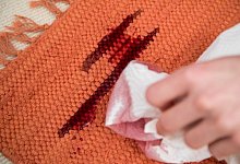 Eine Frau entfernt Rotweinflecken im Teppich mit K&uuml;chenkrepp - Christin Klose/dpa-tmn