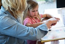 Frau schaut sich mit einem Mädchen ein Kinderbuch an - Christin Klose/dpa-tmn