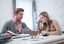 Paar vor Hausmodell und Unterlagen - Christin Klose/dpa-tmn