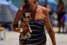 Eine Frau trägt ihren Hund am Strand in den Armen - Diorgenes Pandini/dpa