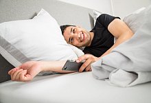 Mann liegt lächelnd morgens im Bett - Christin Klose/dpa-tmn