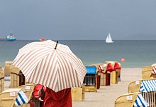 Eine Frau mit Schirm am Strand - Markus Scholz/dpa/dpa-tmn