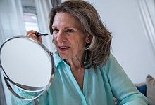 Eine Frau schminkt sich vor einem Schminkspiegel. - Christin Klose/dpa-tmn/dpa