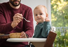 Mann f&uuml;ttert Kleinkind in einem Hochstuhl - Christin Klose/dpa-tmn