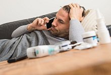 Mann liegt krank auf einem Sofa und telefoniert - Christin Klose/dpa-tmn