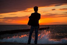 Mann beobachtet am Strand von Ahrenshoop den Sonnenuntergang - Jens Büttner/dpa/dpa-tmn