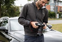 Mann schaut nach dem Fotografieren seines Autos auf Kameradisplay - Christin Klose/dpa-tmn