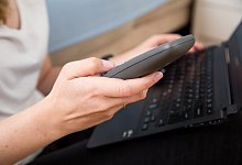 Eine Frau am Laptop wählt auf einem Telefon eine Nummer - Christin Klose/dpa-tmn