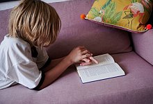 Ein Kind liegt auf dem Sofa und liest - Annette Riedl/dpa/dpa-tmn