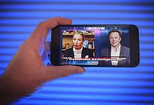 Hand h&auml;lt ein Mobiltelefon auf dem Das Gespr&auml;ch von Alice Weidel mit Elon Musk auf der Plattform X zu sehen ist. *** Hand holds a mobile phone on which Alice Weidel's conversation with Elon Musk on Platform X can be seen. - IMAGO/Guido Schiefer