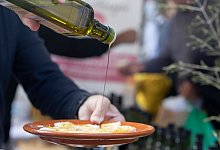 Ein Mann tr&auml;ufelt Oliven&ouml;l auf ein St&uuml;ck Brot - Clara Margais/dpa