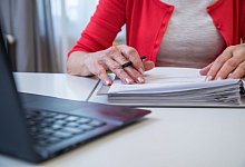 Eine &auml;ltere Frau arbeitet mit Unterlagen am Laptop - Christin Klose/dpa-tmn