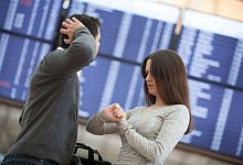Reisende vor Abflug-Anzeige schauen auf die Uhr - Christin Klose/dpa-tmn