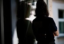 Junge Frau steht in einer Wohnung am Fenster - Fabian Sommer/dpa/dpa-tmn