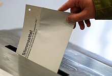 Stimmzettel wird in eine Wahlurne gesteckt - Arne Dedert/dpa