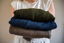 Eine Frau hält einen Stapel Woll-Pullover - Zacharie Scheurer/dpa-tmn