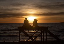 Paar sitzt bei Sonnenuntergang am Strand von Arenal - Clara Margais/dpa/dpa-tmn