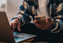 Ein Mann arbeitet am Laptop und hält ein Smartphone in der Hand - Zacharie Scheurer/dpa-tmn