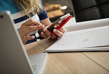 Frau schaut an ihrem Schreibtisch auf ein Smartphone - Christin Klose/dpa-tmn