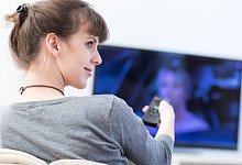 Eine Frau mit Fernbedienung vor dem Fernseher - Foto: Christin Klose/dpa-tmn