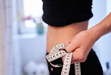 Eine junge Frau h&auml;lt ein Zentimeterma&szlig;band an ihren Bauch - Annette Riedl/dpa/dpa-tmn