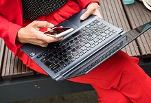 Eine Frau sitzt mit Smartphone und Laptop auf einer Bank - Christin Klose/dpa-tmn